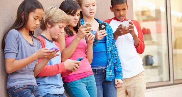 Group Of Children Sitting In Mall Using Mobile Phones